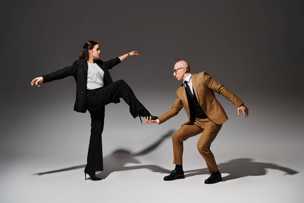 brünette Frau balanciert in High Heels, während sie auf die Hand ihres Tanzpartners im Anzug auf grau tritt - Foto, Bild