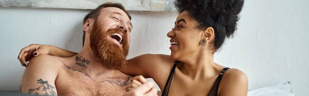happy and tattooed man without shirt laughing with curly african american girlfriend, banner - Photo, Image