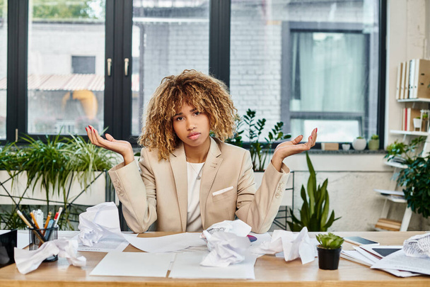 запутанная кудрявая африканская американская деловая женщина за своим столом со смятыми бумагами, стрессом на работе - Фото, изображение