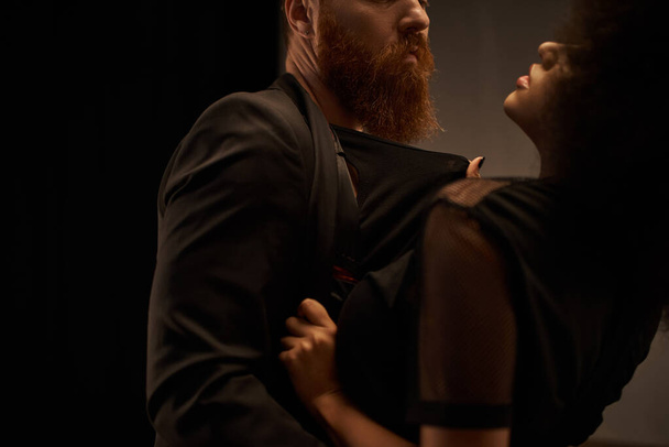 обрезанный африканский американец женщина в платье тянет блейзер бородатый мужчина во время свидания, сексуальная пара - Фото, изображение