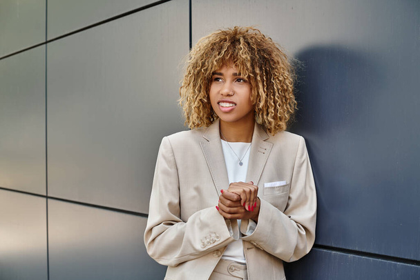 многообещающая африканская американская бизнесвумен в формальной одежде, стоящая рядом с офисным зданием, улыбающаяся - Фото, изображение