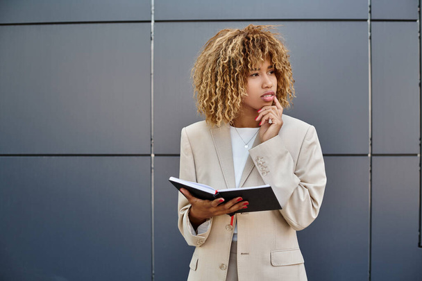 pensive african american businesswoman in formal wear holding her notebook near office building - Photo, Image