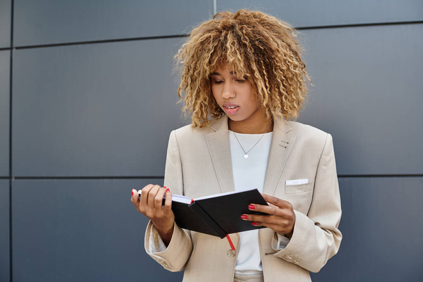 пенсійна афроамериканська бізнес-леді в офісному одязі, дивлячись на її блокнот біля офісної будівлі - Фото, зображення