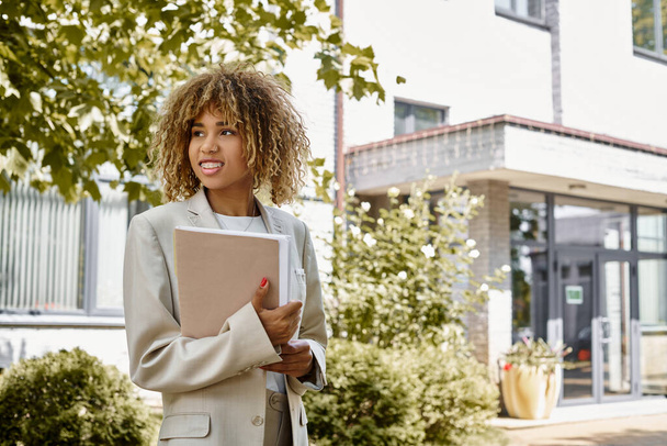 Enthousiaste entrepreneur afro-américain à bretelles debout avec dossier près du bureau par une journée ensoleillée - Photo, image