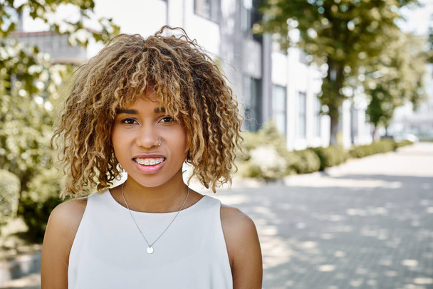 retrato de feliz joven afroamericana mujer con rizos posando en verano cálido día, estilo calle - Foto, imagen