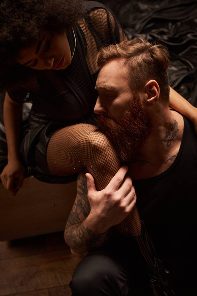 hombre barbudo con tatuajes seduciendo a la joven afroamericana en medias de rejilla con pedrería - Foto, Imagen