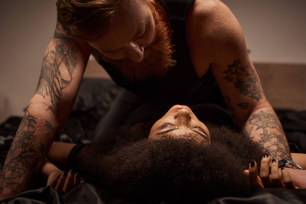 παθιασμένη στιγμή του πολυπολιτισμικού ζευγαριού που κάνει έρωτα στο κρεβάτι, άντρας που κοιτάζει μια Αφροαμερικανή γυναίκα - Φωτογραφία, εικόνα