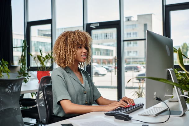 positiver junger afrikanisch-amerikanischer Manager, der im Büro am Schreibtisch vor dem Computermonitor arbeitet - Foto, Bild