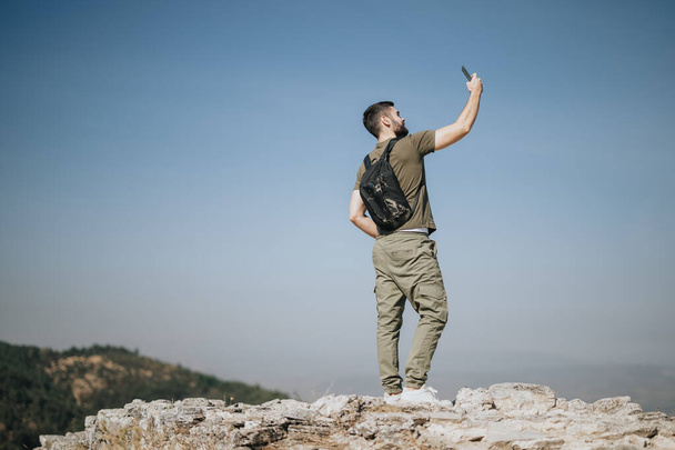 Мужчина-турист делает селфи, стоя на вершине горы. Копирование пространства. - Фото, изображение