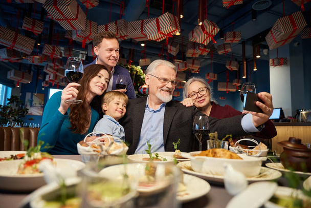 Radostná rodina slaví Nový rok s slavnostní večeři v kavárně dělat selfie na smartphone paměti - Fotografie, Obrázek