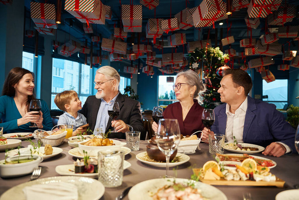 Satisfied family enjoying Christmas dinner together in cozy restaurant spending time together during winter holidays - Photo, Image