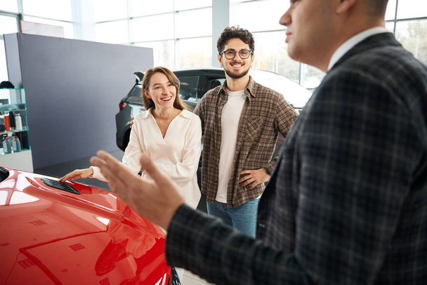 Веселий чоловік і жінка вибирають нову машину, консультуючись з продавцем в дилерському центрі - Фото, зображення