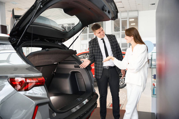 Confident man salesperson selling cars at car dealership presenting special offers to woman client - Photo, Image