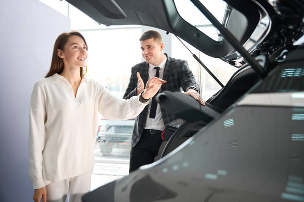 Mujer alegre comprador elegir el coche con la ayuda del vendedor de concesionario femenino comprar nuevo automóvil - Foto, Imagen