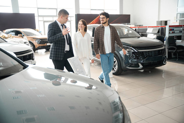 Vendeur et femme à la recherche d'une voiture dans le showroom de voiture en choisissant l'automobile parfaite pour la famille - Photo, image