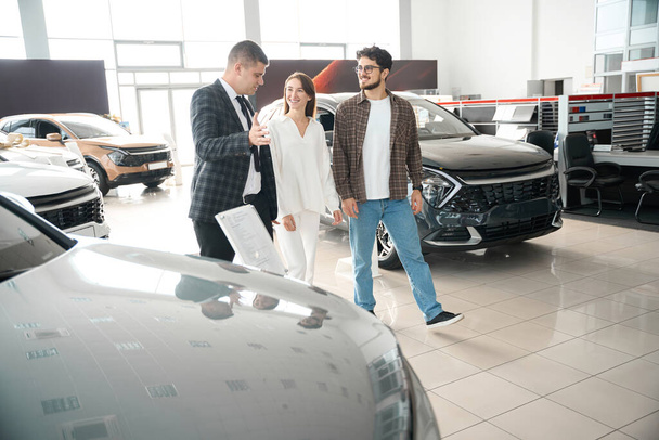 Młoda para rozmawia ze sprzedawcą w salonie samochodowym wybierając samochód do codziennego użytku - Zdjęcie, obraz