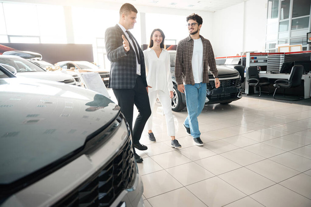 Man and woman walking around dealership choosing car with sales person communicating about new models - Photo, Image