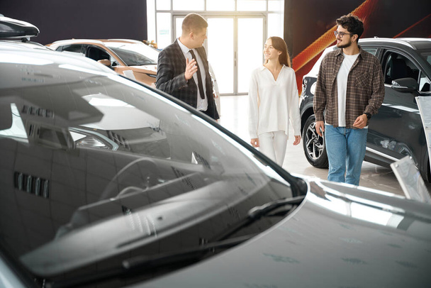 Mężczyzna daje rekomendację dla szczęśliwych klientów rodzinnych do zakupu samochodu w centrum dealerskim - Zdjęcie, obraz