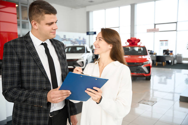 Ικανοποιημένη γυναίκα που αγοράζει νέο αυτοκίνητο υπογραφή σύμβασης με τον πωλητή στην αντιπροσωπεία - Φωτογραφία, εικόνα