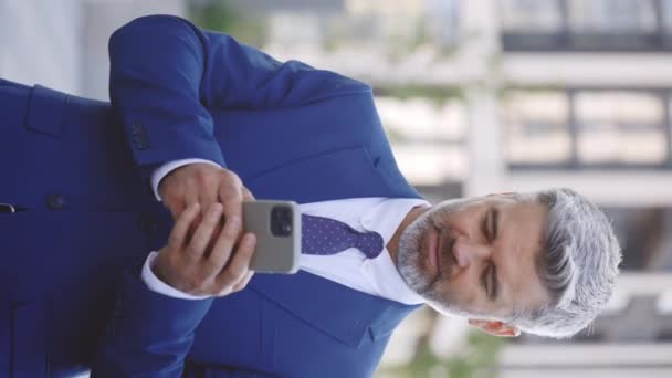 Вертикальное видео. Красивый мужской босс, бородатый человек, ходьба, с помощью смартфона, проведение кофе, и чтение бизнес-новости на смартфоне на открытом воздухе. Концепция технологии и связи - Кадры, видео