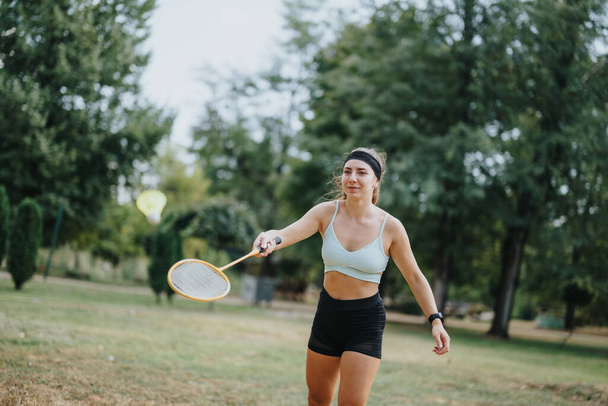 Sporcular parkta badminton oynuyorlar. Arkadaşlar dışarıda eğleniyor. Kızlar sağlıklı yaşam tarzını ve enerjik egzersizleri seviyorlar.. - Fotoğraf, Görsel