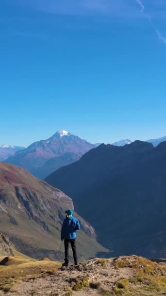 A kék kabátos túrázó a hegyeket nézi. Hegyek és hegyek. Croix du Bonhomme ezredes. Francia Alpok, Franciaország. Légitekintés. Drónrepülők előre. Függőleges videó - Felvétel, videó