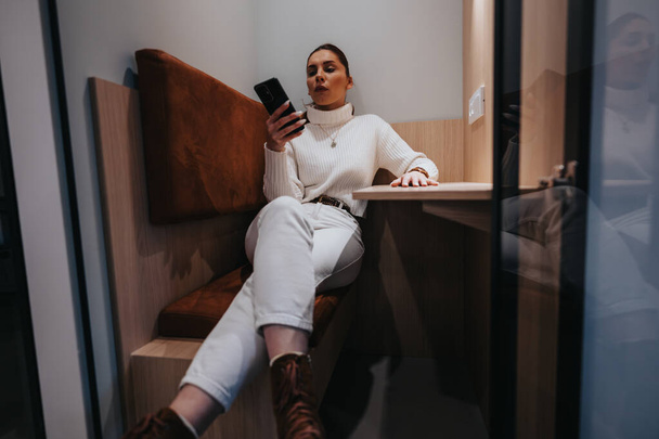 Gorgeous female taking a break from work while having video call meeting sitting in soundproof phone booth. - Photo, Image