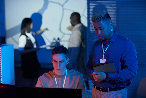 Portrait de deux personnes travaillant dans un centre de contrôle de mission aux tons bleu et rouge futuristes - Photo, image