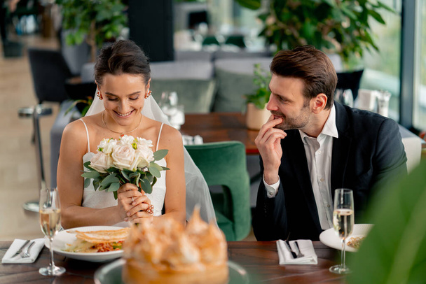 портрет улыбающейся невесты и жениха влюбленных молодоженов на свадьбе в ресторане во время празднования любовного романа - Фото, изображение