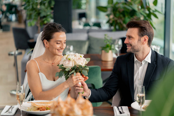 портрет улыбающейся невесты и жениха влюбленных молодоженов на свадьбе в ресторане во время празднования любовного романа - Фото, изображение