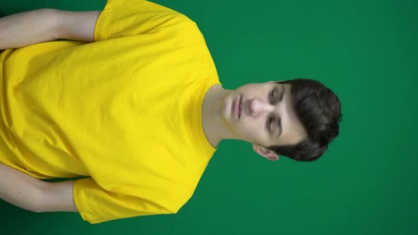 Ο έφηβος με κίτρινα ρούχα κοιτάζει γύρω του και αγγίζει τις άκρες του πλαισίου. Πράσινο φόντο, κάθετο βίντεο. Υψηλής ποιότητας 4k πλάνα - Πλάνα, βίντεο