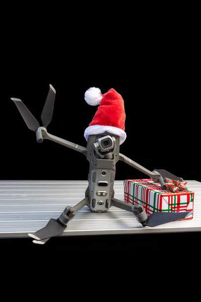 Porträt einer Quadrocopter-Drohne mit Weihnachtsmütze als Weihnachtskonzept auf dunklem Hintergrund, die das Friedenszeichen gibt. - Foto, Bild