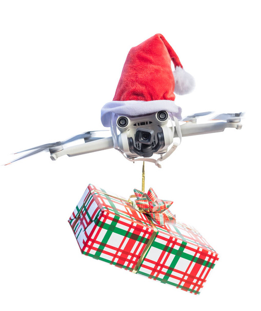 Dron koncept nosí Santa klobouk a drží zabalený dárek pro dodání izolované na bílém pozadí. - Fotografie, Obrázek