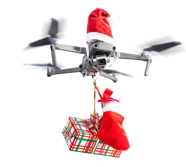 Dron koncept nosí Santa klobouk a drží zabalený dárek pro dodání izolované na bílém pozadí. - Fotografie, Obrázek