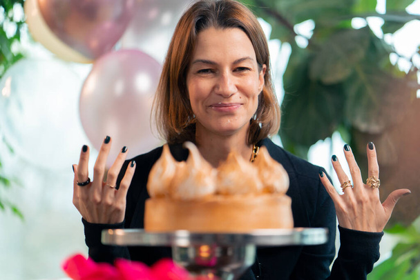 портрет щасливої дівчини, яка з задоволенням їсть святковий торт і лиже пальці під час вечірки в ресторані з подарунками - Фото, зображення