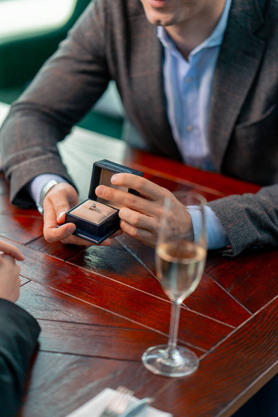 egy közeli felvétel egy étteremről, ahol egy férfi megkéri a szerelme kezét egy doboz gyűrűvel és megkéri a kezét. - Fotó, kép