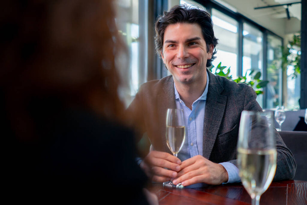 portré egy mosolygós jóképű férfiról, aki egy étteremben ül egy lánnyal egy pohár pezsgővel. - Fotó, kép
