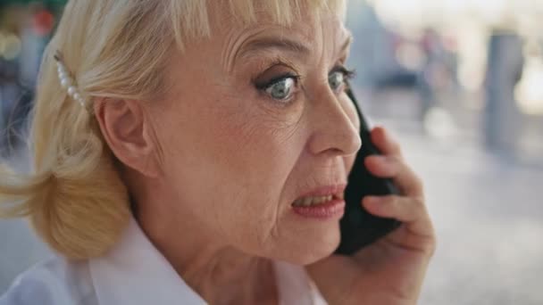 Nahaufnahme nervöser Rentner, der mit seinem Smartphone im Freien negative Emotionen ausdrückt. Wütende ältere Geschäftsfrau, die sich per Handy über unzufriedene Arbeitsbedingungen streitet. Alte Dame ruft auf Handy. - Filmmaterial, Video