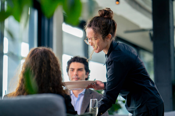 une fille serveur sert commandes aux clients le concept d'hospitalité et de service dans un restaurant de grande classe - Photo, image