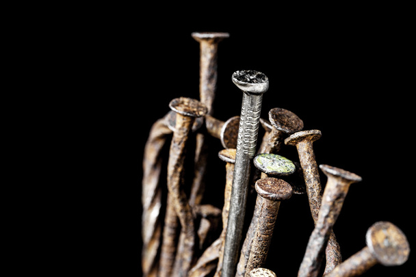 The leadership concept. New steel nail over group of old rust nails on a black background. - Fotoğraf, Görsel