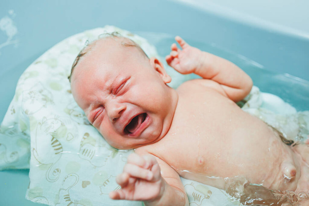 Un neonato sta piangendo in un bagno. Bagnare un neonato in una vasca da bagno. Il primo bagno di un neonato. - Foto, immagini