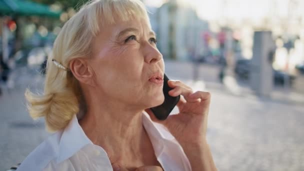 Mulher idosa sorrindo chamando o telefone celular na rua ensolarada fechar. Retrato de pensionista bonito elegante falando no smartphone em pé ao ar livre. Velha senhora feliz desfrutar de comunicação telefônica fora. - Filmagem, Vídeo