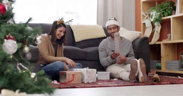 Kerstboom, koppel en cadeau met papieren verpakking en feest thuis. Happy, conversatie en jongeren met cadeau, doos en communicatie in een woonkamer voor vakantie met liefde en geven. - Video
