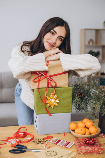Όμορφη ευτυχισμένη γυναίκα τυλίγει και κρατά χριστουγεννιάτικα δώρα στο σπίτι - Φωτογραφία, εικόνα