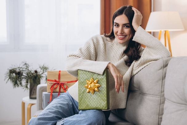 Belle femme heureuse déballer des cadeaux de Nouvel An ou de Noël à la maison sur le canapé - Photo, image