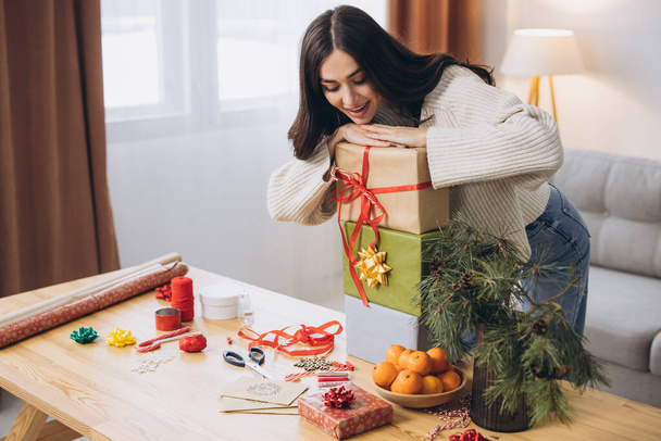 Красивая счастливая женщина упаковывает и держит рождественские подарки дома - Фото, изображение