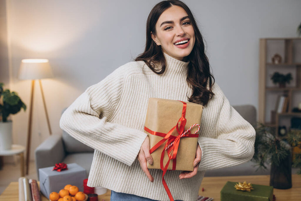 Красивая счастливая женщина упаковывает и держит рождественские подарки дома - Фото, изображение