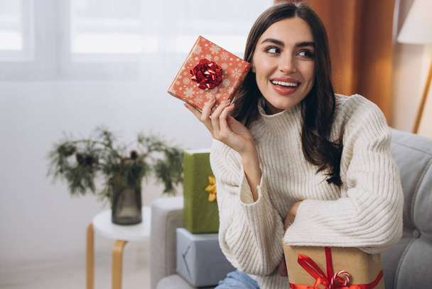 Schöne glückliche Frau packt Neujahrs- oder Weihnachtsgeschenke zu Hause auf dem Sofa aus - Foto, Bild