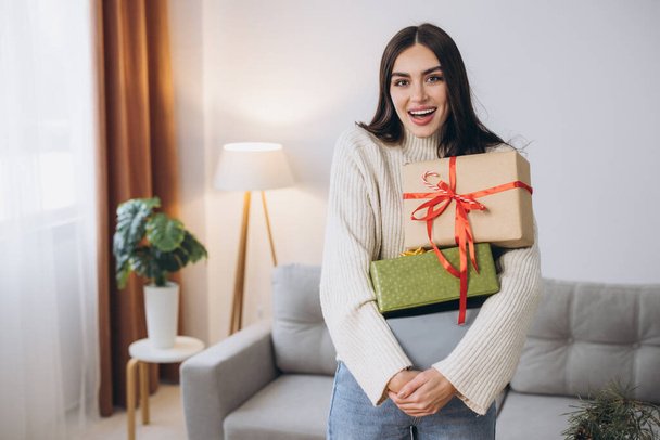 Όμορφη ευτυχισμένη γυναίκα τυλίγει και κρατά χριστουγεννιάτικα δώρα στο σπίτι - Φωτογραφία, εικόνα