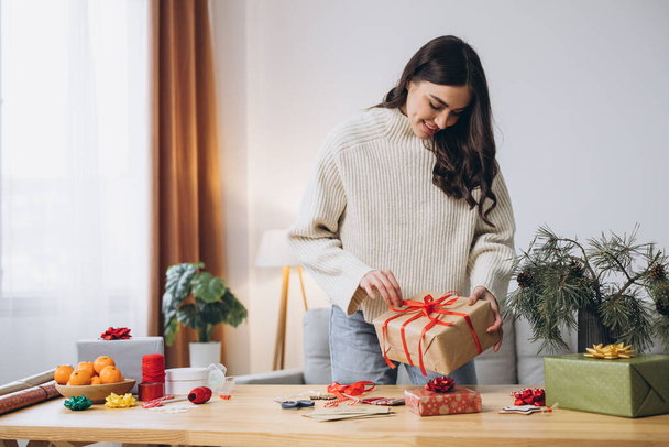 Kobieta pakująca pudełka świąteczne, zamyka. Nieprzygotowane prezenty na białym stole z elementami wystroju i przedmiotów Boże Narodzenie lub Nowy rok DIY opakowania Concept. - Zdjęcie, obraz